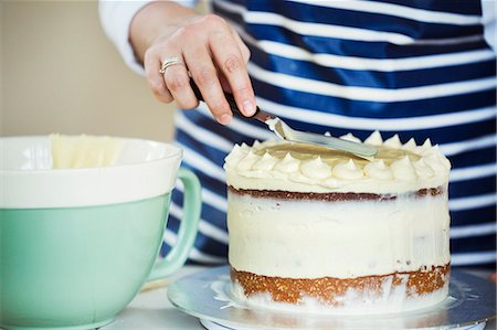 simsearch:6118-08971487,k - Close up of person wearing a blue and white stripy apron spreading cream over the top of a cake. Stockbilder - Premium RF Lizenzfrei, Bildnummer: 6118-08971507