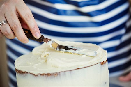 simsearch:6118-08971487,k - Close up of person wearing a blue and white stripy apron spreading cream over the top of a cake. Stockbilder - Premium RF Lizenzfrei, Bildnummer: 6118-08971506