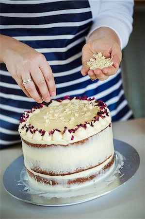 Close up of person wearing a blue and white stripy apron sprinkling white chocolate stars on a cake. Stock Photo - Premium Royalty-Free, Code: 6118-08971510