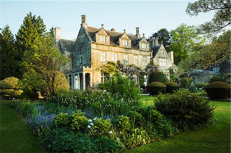 Exterior view of a 17th century Cotswold stone country house from a garden with flower beds, shrubs and trees. Photographie de stock - Premium Libres de Droits, Code: 6118-08971531