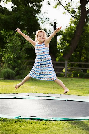 simsearch:6118-08971638,k - Girl in a sundress jumping on a trampoline set in the ground, in a garden. Photographie de stock - Premium Libres de Droits, Code: 6118-08971645