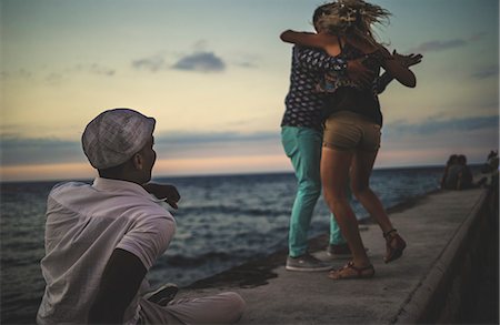 simsearch:6118-08991633,k - Two people dancing on a sea wall watched by a man facing the ocean. Stock Photo - Premium Royalty-Free, Code: 6118-08991355