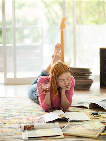 A woman lying on the floor holding a drink and reading a magazine. Stock Photo - Premium Royalty-Free, Code: 6118-08991375