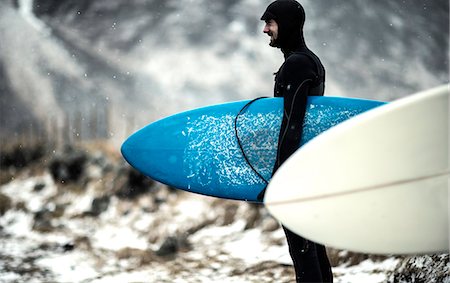 simsearch:6118-09039316,k - A surfer wearing a wetsuit and carrying surfboards standing on a snowy beach with mountains behind. Foto de stock - Sin royalties Premium, Código: 6118-08991413