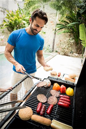 simsearch:6118-08991513,k - A man holding tongs and turning food on a barbecue. Foto de stock - Royalty Free Premium, Número: 6118-08991505