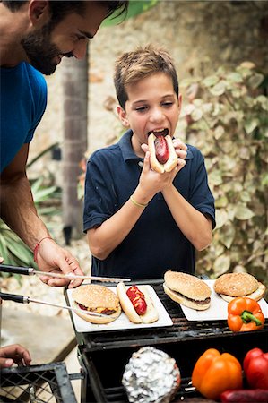 simsearch:6118-08991513,k - A boy and a man standing at an open barbecue eating. Foto de stock - Royalty Free Premium, Número: 6118-08991515