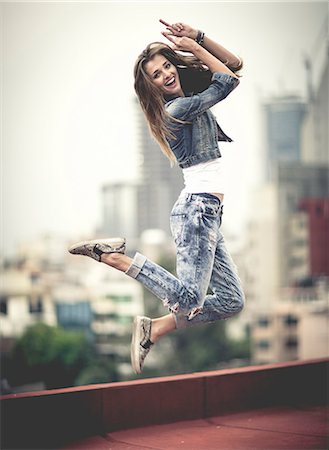 simsearch:6118-09039292,k - Young woman jumping on a rooftop with her arms raised. Foto de stock - Sin royalties Premium, Código: 6118-08991535