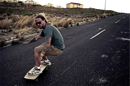 simsearch:6118-09039293,k - A young man skateboarding on a road. Photographie de stock - Premium Libres de Droits, Code: 6118-08991652