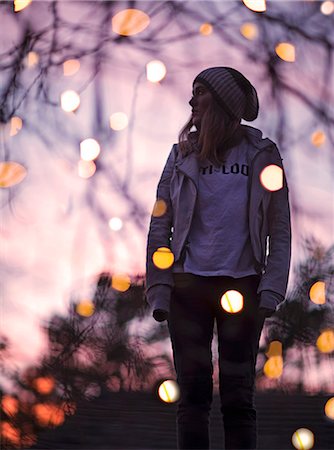 fall - Young woman standing among trees at dusk, fairy lights around her, turning her head. Stock Photo - Premium Royalty-Free, Code: 6118-08991668