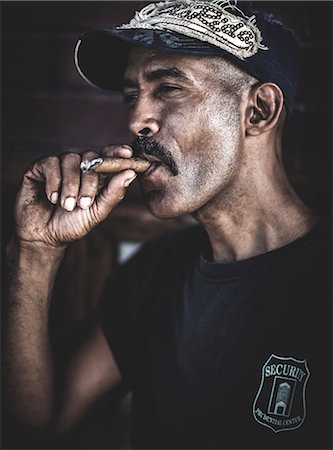 A man wearing a baseball cap smoking a cigar. Photographie de stock - Premium Libres de Droits, Code: 6118-08991687