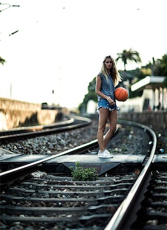 simsearch:6118-09039293,k - Young woman standing on railway tracks holding a basketball. Photographie de stock - Premium Libres de Droits, Code: 6118-08991627