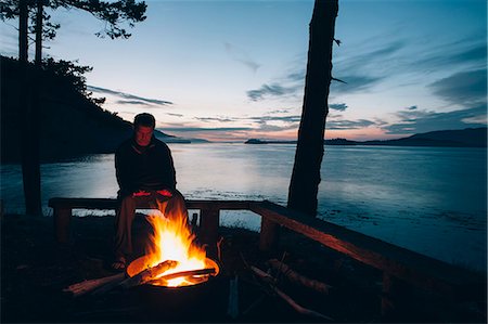 simsearch:6118-09112089,k - Man sitting by campfire at dusk, San Juan Islands in the distance, Washington, USA. Photographie de stock - Premium Libres de Droits, Code: 6118-08910377