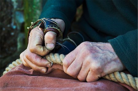 Close up of man wearing sailmakers palms, holding a sail and rope in a sailmaker's workshop. Photographie de stock - Premium Libres de Droits, Code: 6118-08928167