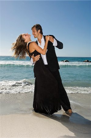 simsearch:6116-08945685,k - man in suit dancing with blond woman in black evening gown on a sandy beach. Fotografie stock - Premium Royalty-Free, Codice: 6118-08928195