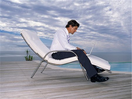 swimming pool side furniture images - A man in a white shirt and black trousers in a sun lounger chair with a laptop on his lap. Foto de stock - Sin royalties Premium, Código: 6118-08928264
