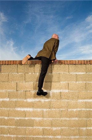 Rear view of man wearing a suit climbing over yellow brick wall. Stock Photo - Premium Royalty-Free, Code: 6118-08928207