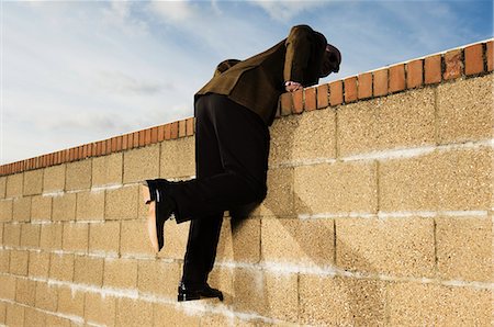 Side view of man wearing a suit climbing over yellow brick wall. Stock Photo - Premium Royalty-Free, Code: 6118-08928206