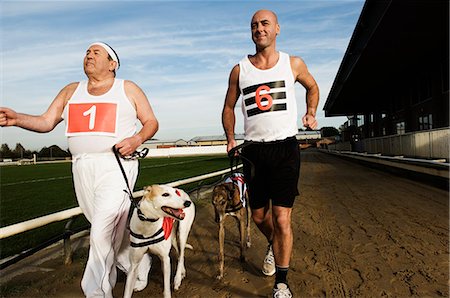 simsearch:400-07795226,k - Two men in sportswear running on a racetrack with two greyhounds on leads. Foto de stock - Royalty Free Premium, Número: 6118-08928208