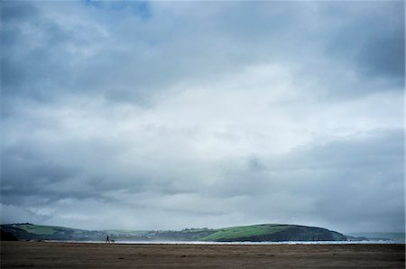 Silhouette of a dog walker and dog on a sandy beach under an overcast sky. Headland and coastline. Photographie de stock - Premium Libres de Droits, Code: 6118-09059467