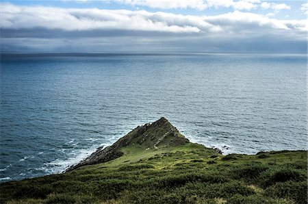 simsearch:6118-09147966,k - The view from above of a sharp ridge and steep hillside on a headland reaching into the sea. Waves breaking under a cloudy sky. Photographie de stock - Premium Libres de Droits, Code: 6118-09059466