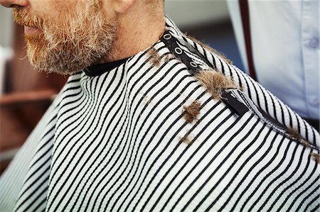 simsearch:400-08955424,k - A man sitting in the barber's chair wearing a striped cape with hair trimmings on his shoulder. Stock Photo - Premium Royalty-Free, Code: 6118-09059691