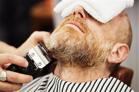 simsearch:400-08955424,k - A customer sitting in the barber's chair, with a hot towel on his face, and a barber trimming his beard wth an electric trimmer. Stockbilder - Premium RF Lizenzfrei, Bildnummer: 6118-09059694