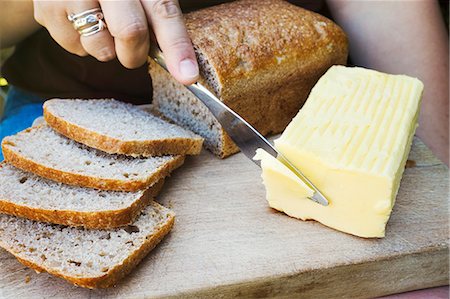 spreading butter on bread - A person with a knife slicing through a block of butter for a sliced bread loaf. Stock Photo - Premium Royalty-Free, Code: 6118-09059759