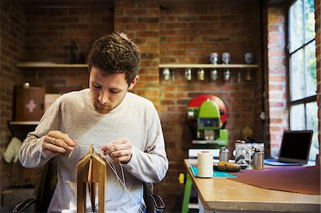 simsearch:6118-09059818,k - A craftsman seated at a bench in a small workshop, threading string through a wooden object. Stock Photo - Premium Royalty-Free, Code: 6118-09059814