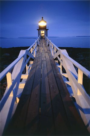 Illuminated wooden walkway towards lighthouse in the evening. Foto de stock - Sin royalties Premium, Código: 6118-09076395