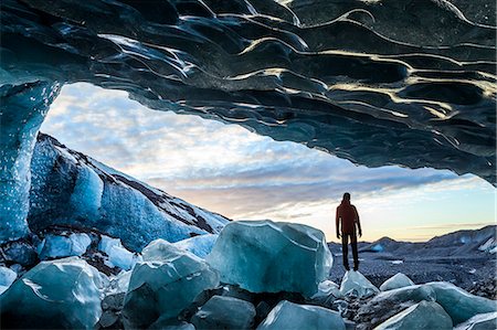 Rear view silhouette of person standing on ice rock at the entrance to a glacial ice cave. Stock Photo - Premium Royalty-Free, Code: 6118-09076552