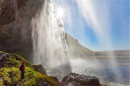 simsearch:6118-08827494,k - person standing on the edge of rock near a waterfall cascade over a sheer cliff. Fotografie stock - Premium Royalty-Free, Codice: 6118-09076536