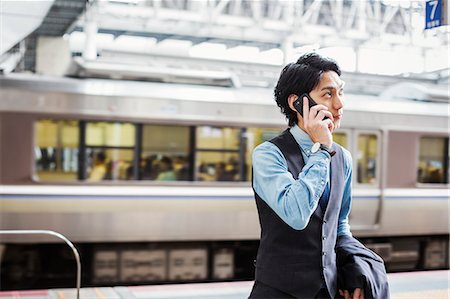 Businessman wearing blue shirt and vest standing on train station platform, talking on mobile phone. Photographie de stock - Premium Libres de Droits, Code: 6118-09079188