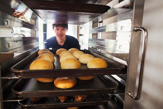 Man working in a bakery, placing large trays with freshly baked rolls on a trolley. Photographie de stock - Premium Libres de Droits, Le code de l’image : 6118-09079269
