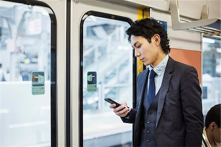 Businessman wearing suit standing on a commuter train, holding mobile phone. Photographie de stock - Premium Libres de Droits, Code: 6118-09079203