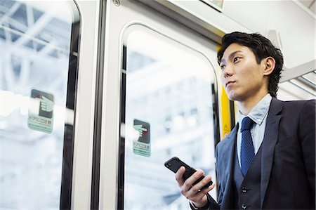 Businessman wearing suit standing on a commuter train, holding mobile phone. Photographie de stock - Premium Libres de Droits, Code: 6118-09079204