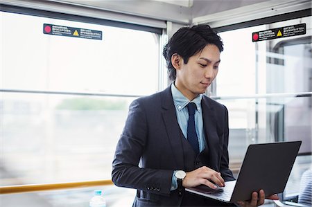 simsearch:640-01358423,k - Businessman wearing suit standing on a commuter train, holding laptop. Foto de stock - Royalty Free Premium, Número: 6118-09079212