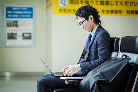 Businessman wearing suit and glasses sitting at train station, working on laptop. Foto de stock - Sin royalties Premium, Código: 6118-09079232
