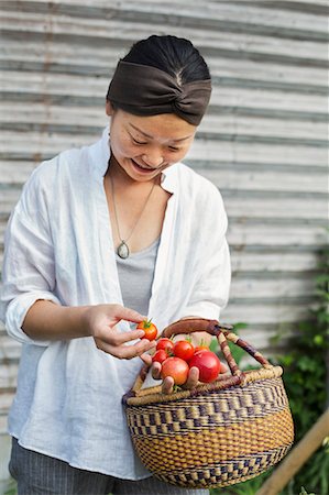 simsearch:6118-09079349,k - Smiling woman standing outdoors, holding basket and freshly picked tomatoes. Stock Photo - Premium Royalty-Free, Code: 6118-09079356