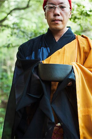 simsearch:6118-09079556,k - Buddhist monk with shaved head wearing black and yellow robe, standing outdoors, holding singing bowl. Foto de stock - Sin royalties Premium, Código: 6118-09079382