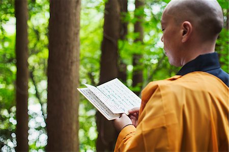 simsearch:649-08633038,k - Side view of Buddhist monk with shaved head wearing black and yellow robe, standing outdoors, holding prayer text. Stock Photo - Premium Royalty-Free, Code: 6118-09079387