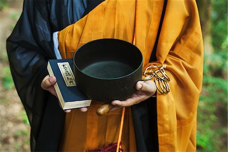 simsearch:6118-09079564,k - Close up of Buddhist monk wearing black and yellow robe, standing outdoors, holding prayer book and singing bowl. Fotografie stock - Premium Royalty-Free, Codice: 6118-09079384
