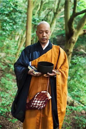 simsearch:6118-09079556,k - Buddhist monk with shaved head wearing black and yellow robe, standing outdoors, holding prayer book and singing bowl. Foto de stock - Sin royalties Premium, Código: 6118-09079385
