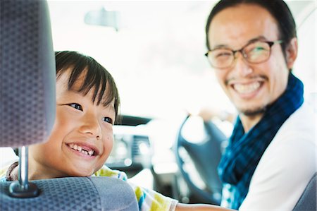 Man wearing glasses and boy sitting in a car, smiling at camera. Stock Photo - Premium Royalty-Free, Code: 6118-09079322
