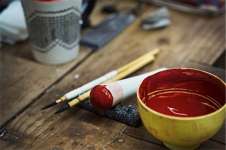 Close up materials in a Japanese porcelain workshop, bowl with red paint, pestle and paintbrushes. Photographie de stock - Premium Libres de Droits, Code: 6118-09079452