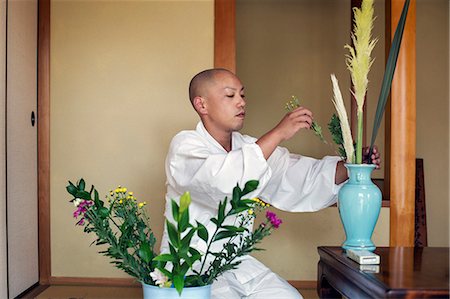 photographs japan temple flowers - Buddhist monk with shaved head wearing white robe kneeling on floor, arranging flowers in blue vase. Stock Photo - Premium Royalty-Free, Code: 6118-09079409