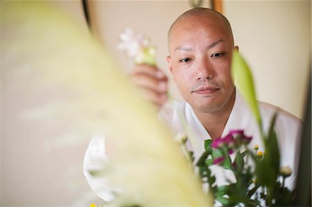 simsearch:6118-09079564,k - Close up of Buddhist monk with shaved head wearing white robe arranging flowers in a vase. Fotografie stock - Premium Royalty-Free, Codice: 6118-09079410