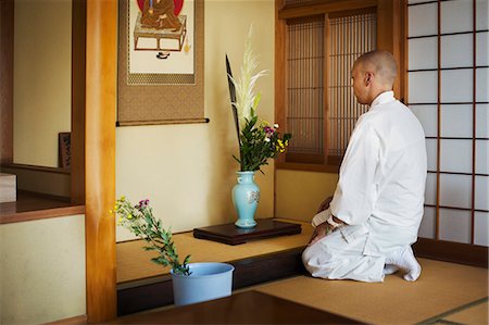 simsearch:6118-09079556,k - Side view of Buddhist monk with shaved head wearing white robe kneeling in front of vase with flowers. Foto de stock - Sin royalties Premium, Código: 6118-09079411