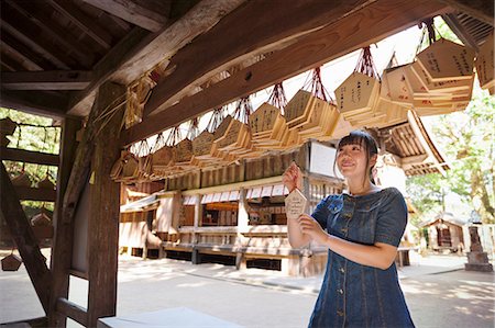 simsearch:693-03313498,k - Young woman wearing blue dress looking at wooden fortune telling plaques at Shinto Sakurai Shrine, Fukuoka, Japan. Foto de stock - Royalty Free Premium, Número: 6118-09079545