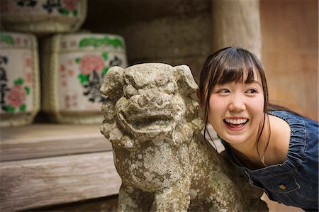 simsearch:862-06825843,k - Young woman wearing blue dress standing next to stone sculpture of lion at Shinto Sakurai Shrine, Fukuoka, Japan. Stock Photo - Premium Royalty-Free, Code: 6118-09079558