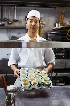 simsearch:6118-09079603,k - Chef working in the kitchen of a Japanese sushi restaurant, holding tray with small bowls of food. Stock Photo - Premium Royalty-Free, Code: 6118-09079602